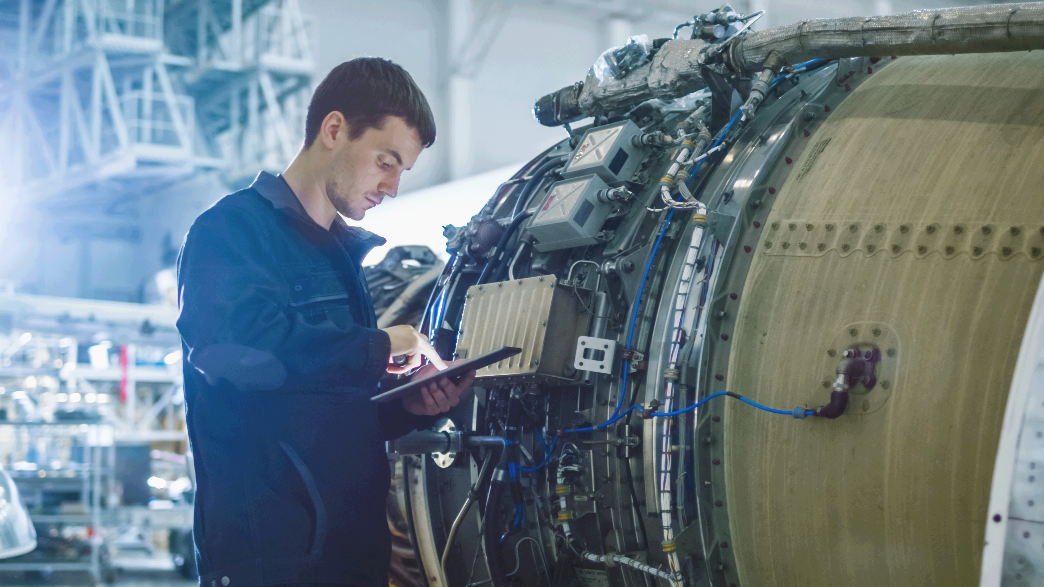 Un homme portant une veste sombre inspecte un gros moteur à réaction à l’intérieur d’une installation industrielle, à l’aide d’une tablette, tout en se tenant à côté de la machine avec des fils et des composants exposés. Un homme portant une veste sombre inspecte un gros moteur à réaction à l'intérieur d'une installation industrielle, à l'aide d'une tablette, tout en se tenant à côté de la machine avec des fils et des composants exposés.