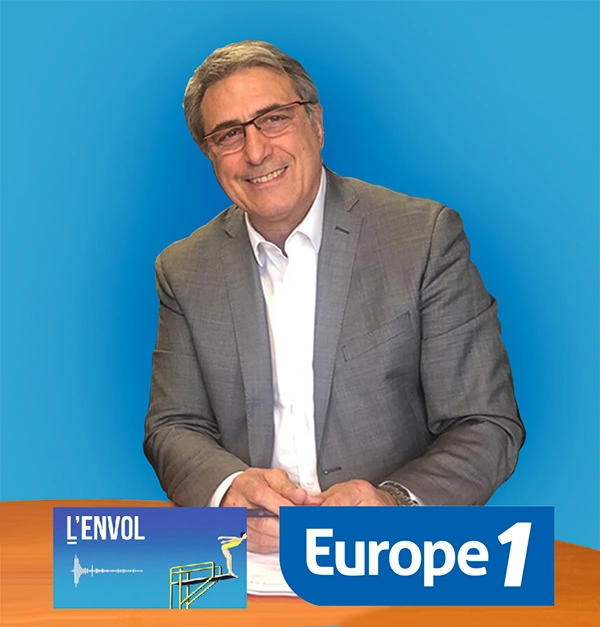 Un homme souriant, vêtu d'un costume gris et d'une chemise blanche, est assis à une table et tient un stylo. Au premier plan, des graphiques représentant LENVOL et le logo d'Europe 1 sur fond bleu.