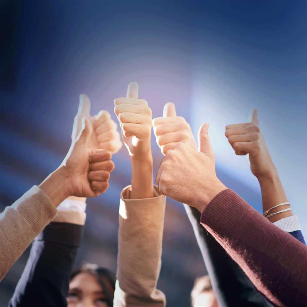 Un groupe de personnes levant les mains et levant les pouces ensemble, sur fond extérieur flou avec un ciel bleu lumineux.
