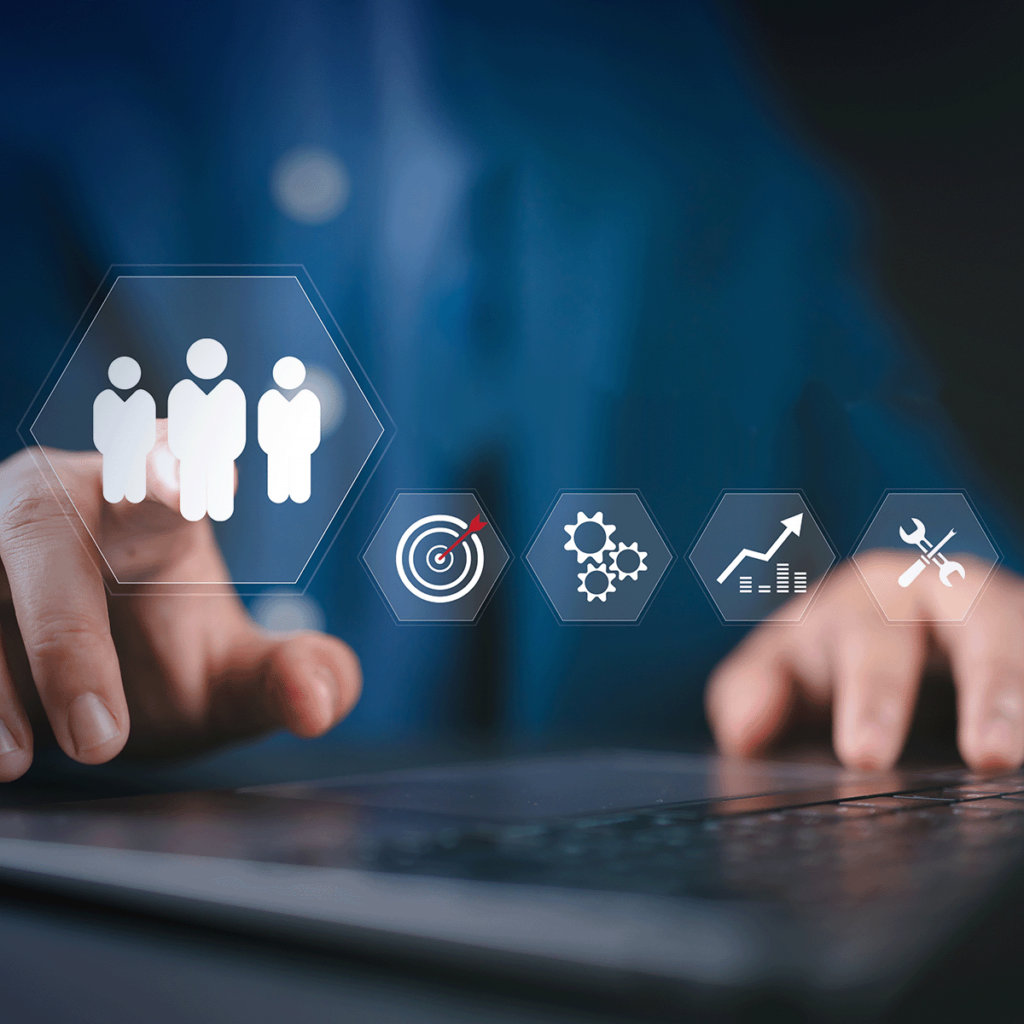 Une personne utilise un ordinateur portable tout en touchant des icônes numériques montrant des personnes, une cible, des engrenages, un graphique ascendant et des outils, représentant des concepts de stratégie commerciale et de technologie.