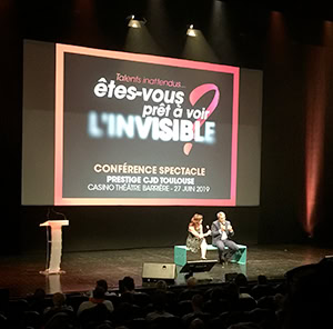 Deux personnes s'assoient et parlent sur scène devant un public. Derrière eux, un grand écran diffuse « êtes-vous prêt à voir l’invisible ? » – une conférence Prestige du CJD Toulouse, mettant en lumière Talents inattendus au Casino Théâtre Barrière, le 27 juin 2019.