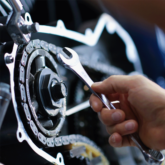 Une main utilise une clé pour ajuster un boulon sur un mécanisme de chaîne métallique, faisant peut-être partie d'une machine ou d'un moteur, mettant en évidence des travaux d'entretien ou de réparation.