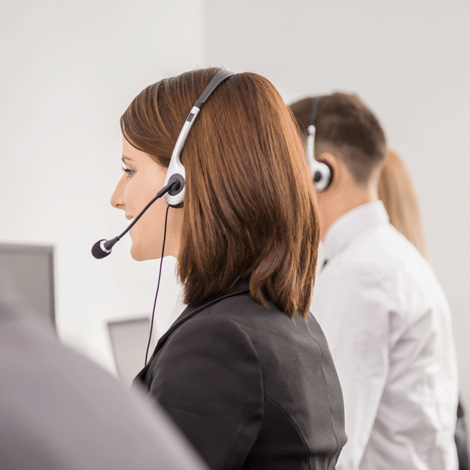 Plusieurs représentants du service client portant des casques sont assis en rangée à leur bureau dans un bureau lumineux, se concentrant sur leurs écrans d'ordinateur pendant qu'ils travaillent.
