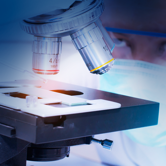 Une personne portant un masque facial examine attentivement un échantillon au microscope, les lentilles du microscope et la lame étant parfaitement nettes.