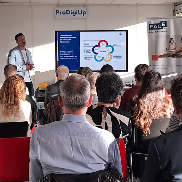 Un homme fait une présentation devant un public dans une salle lumineuse. Un grand écran affiche un diagramme d'entreprise. Des bannières portant les logos de ProDigiUp et de FACE sont visibles, indiquant un événement professionnel ou éducatif axé sur l'inclusion.